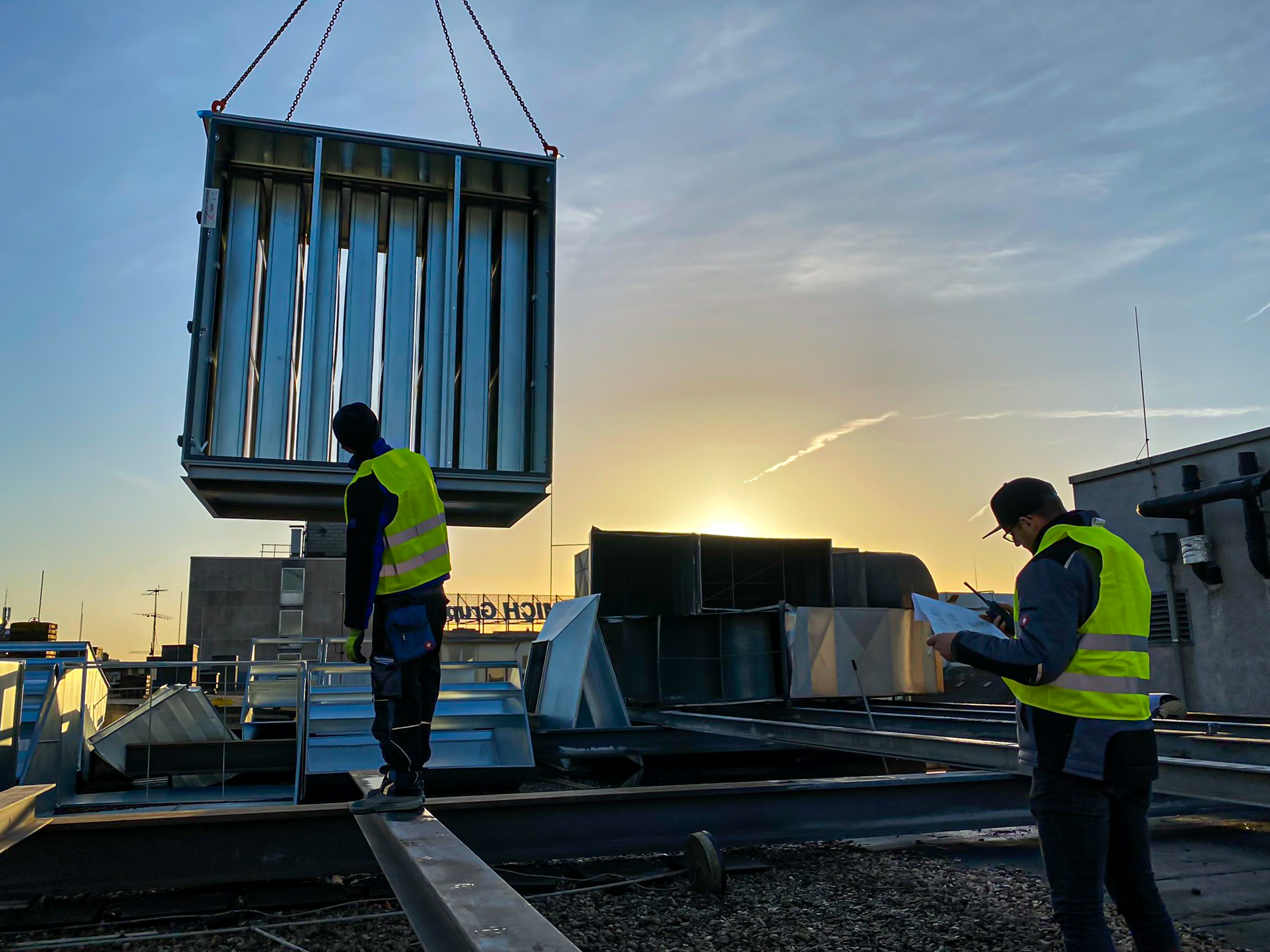 Kranmontage einer Lüftungsanlage auf einem Dach bei Sonnenuntergang